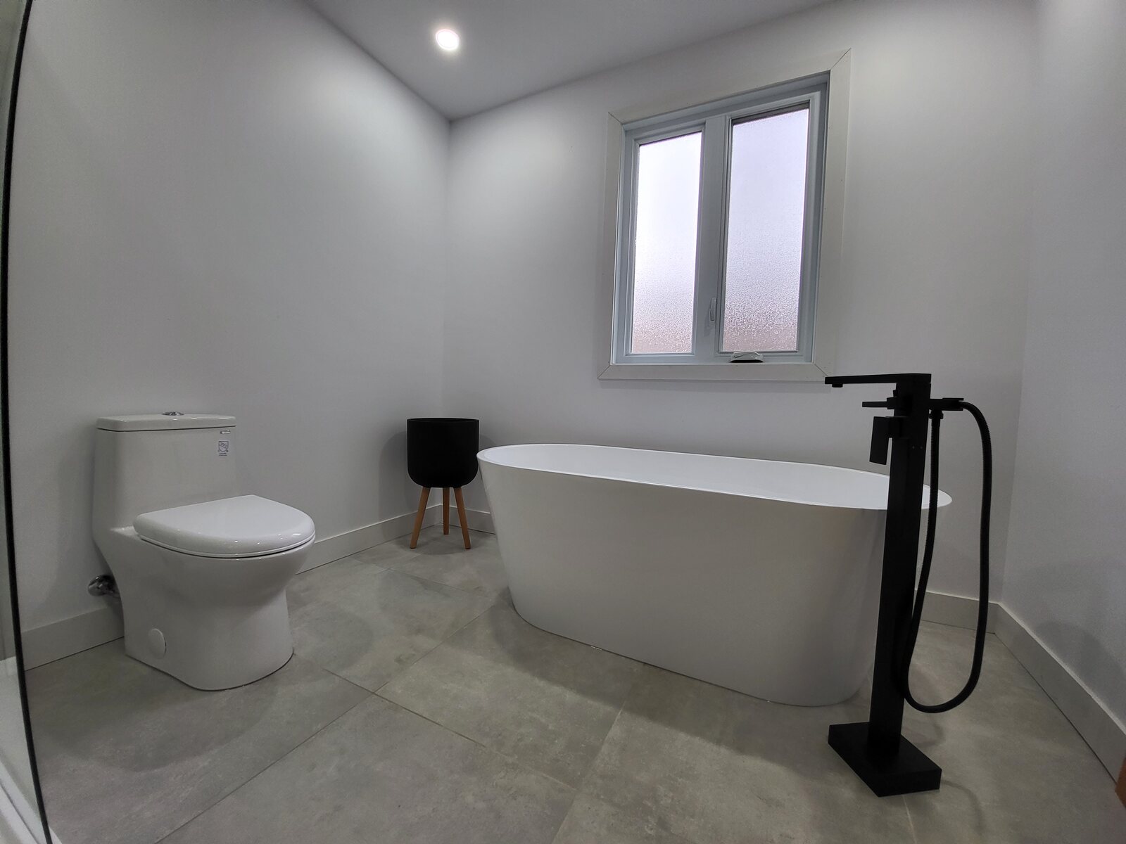 Salle de bain avec bain autoportant blanc, robinetterie noire et plancher gris