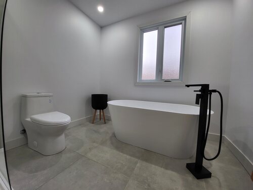 Salle de bain avec bain autoportant, robinetterie noire et plancher gris