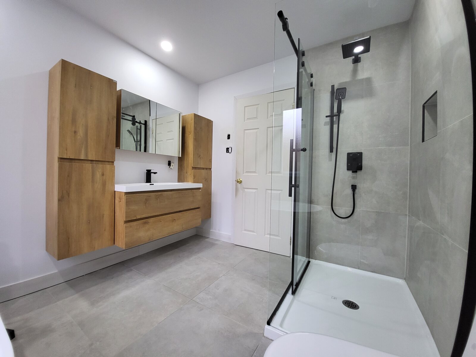 Salle de bain avec vanité en bois, grande douche vitrée et céramique grise