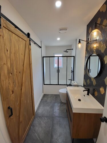 Salle de bain avec vanité noire, mur hexagonal et douche vitrée