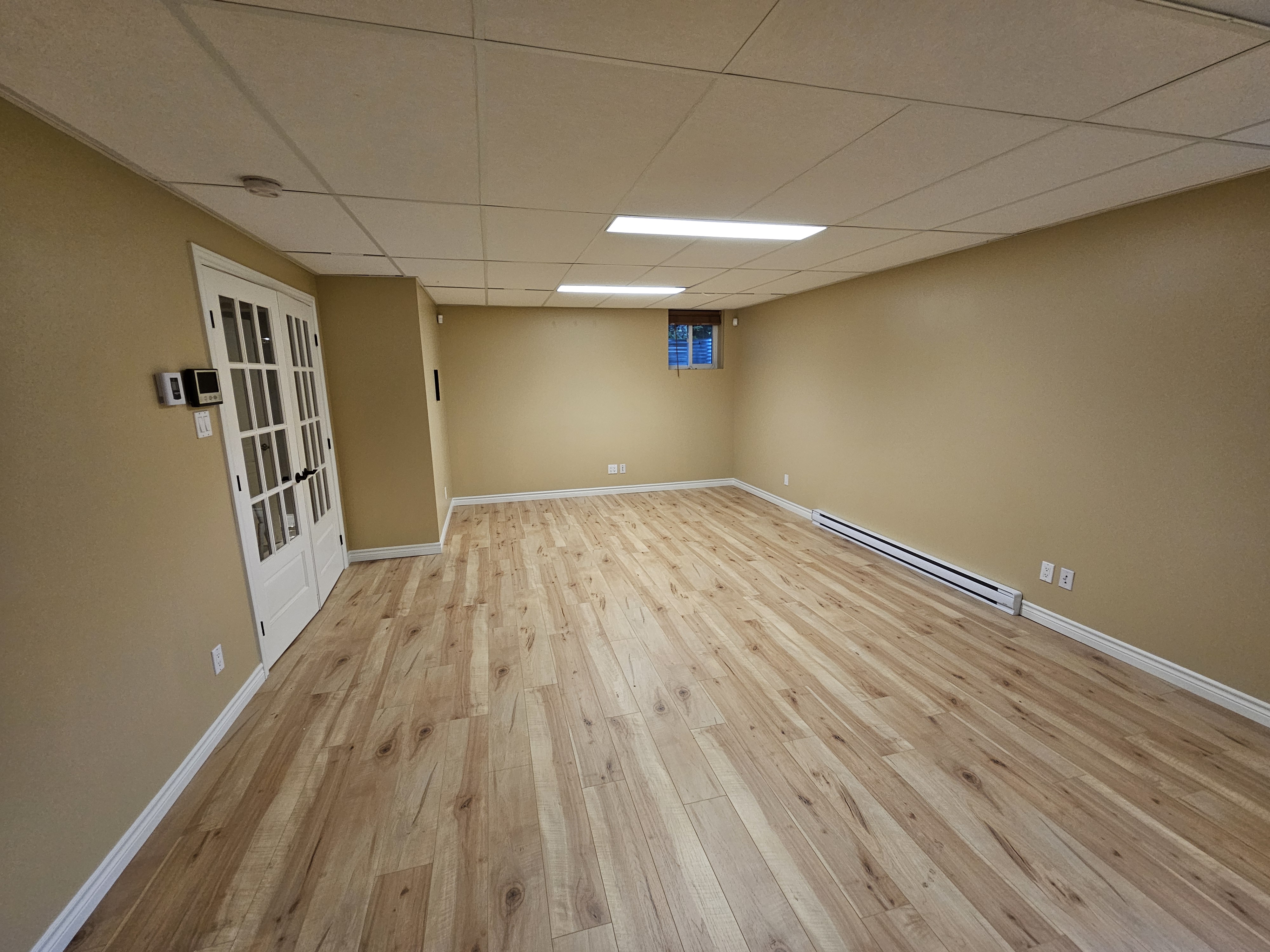 Salle polyvalente au sous-sol avec portes françaises, plancher clair et éclairage au plafond