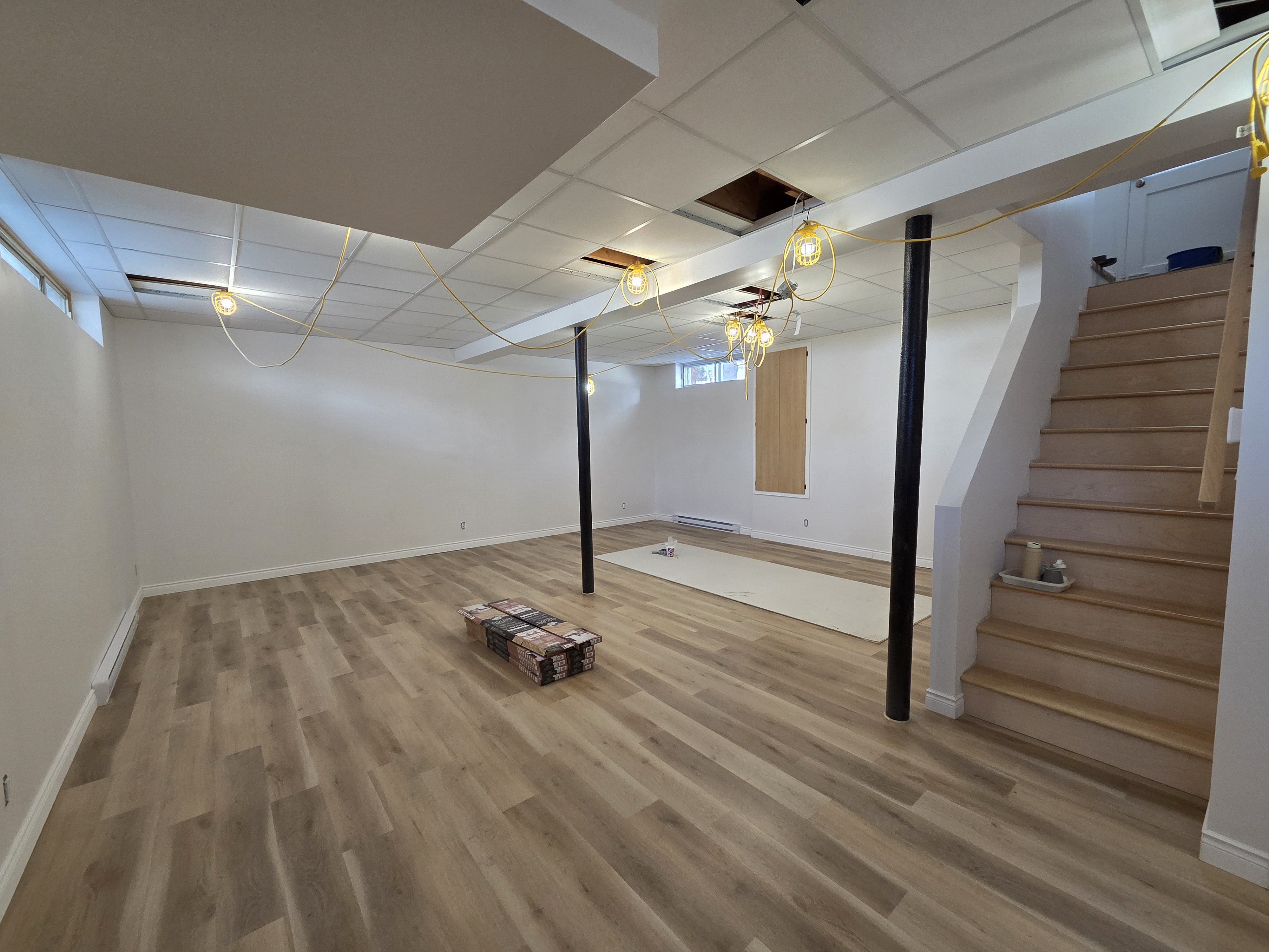 Sous-sol en cours d’aménagement avec escalier, câblage et plafond suspendu