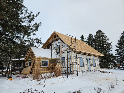 Chantier d’ajout d’étage : charpente montée au-dessus d’une maison en hiver
